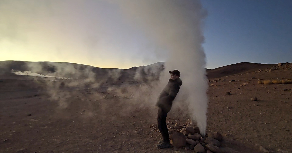 Person leaning into steam from a geyser at sunrise in Bolivia