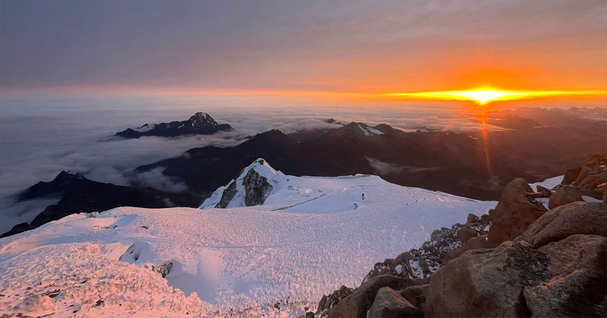 View from the summit of Huayna Potosi as the sun rises, painting the horizon in warm colors.