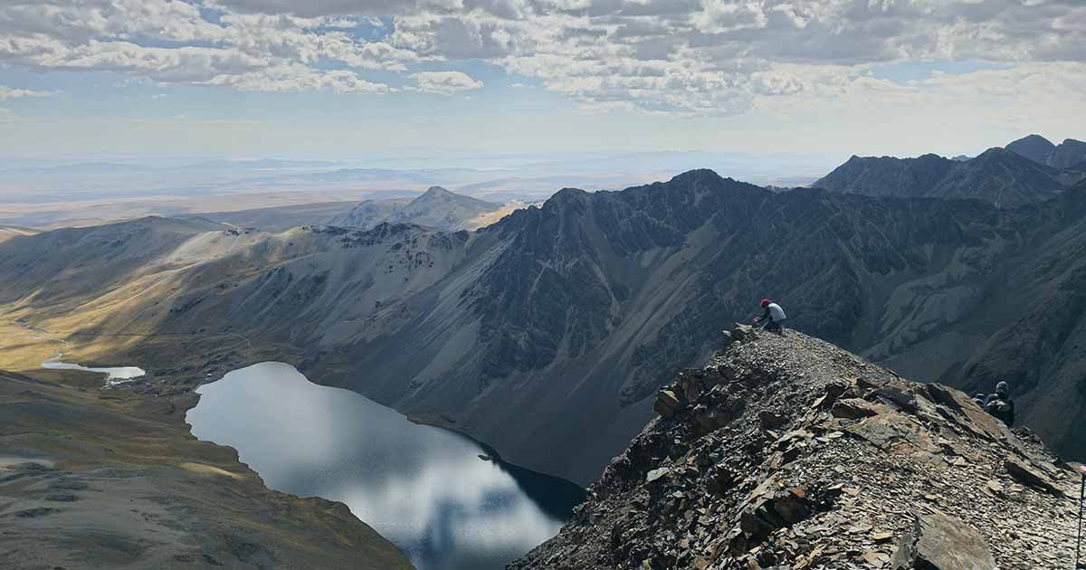 Hiker standing on rocky terrain at the summit of Pico Austria with mountains in the background