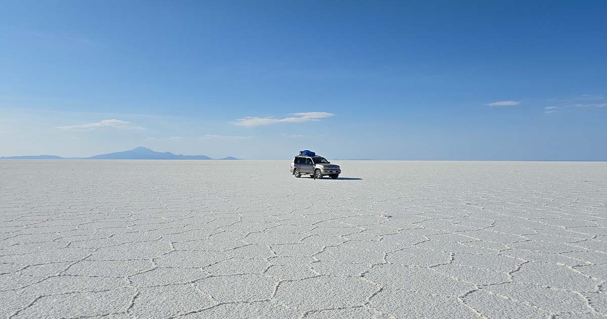 The endless salt flats of Salar de Uyuni under a clear blue sky with a car.