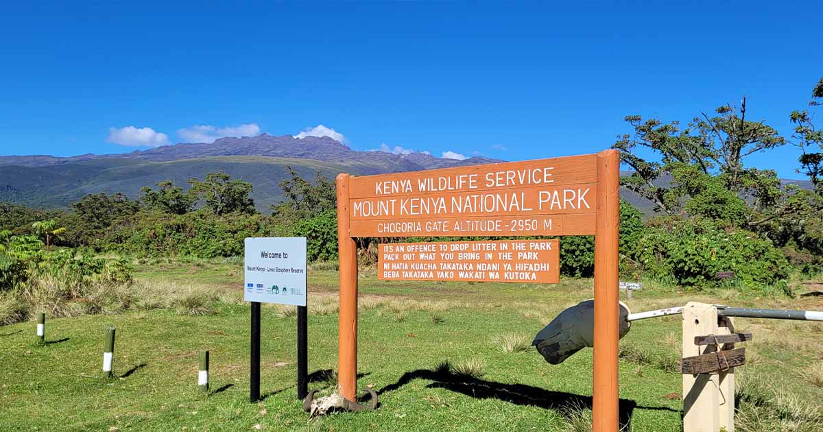 A signpost at the entrance of Mount Kenya National Park at the Chogoria Gate, indicating an altitude of 2950 meters with a clear blue sky and lush greenery in the background