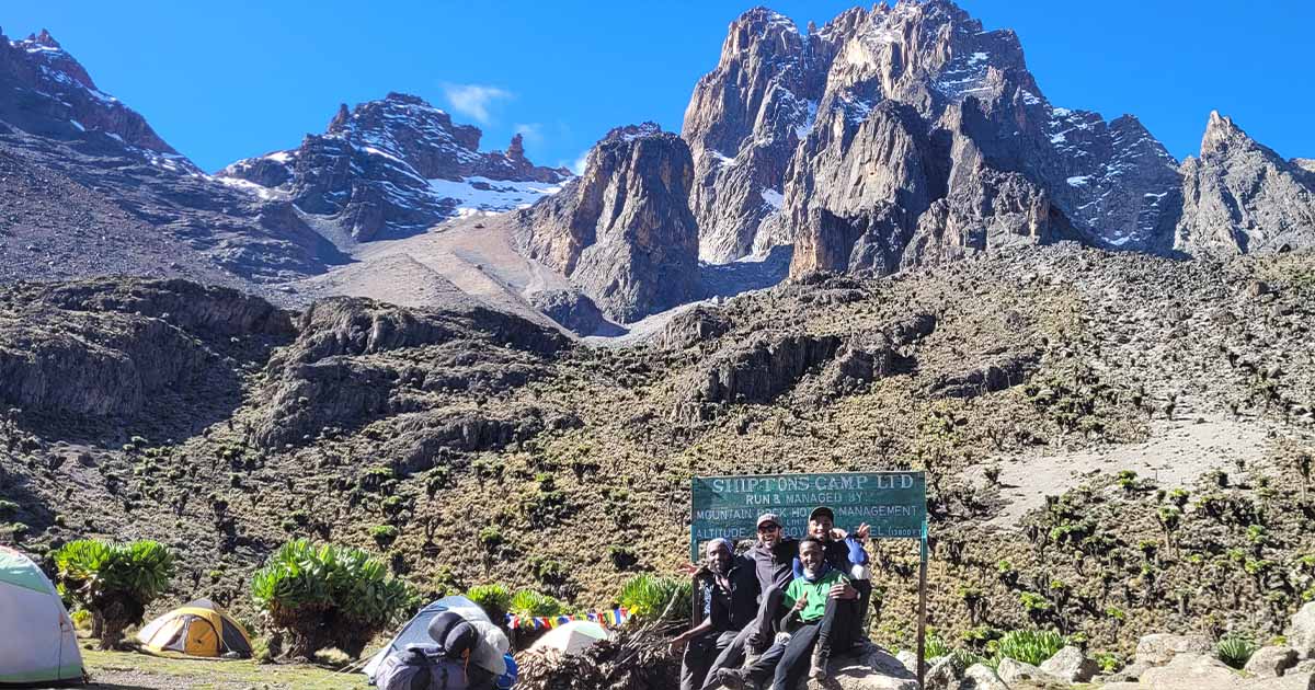 A group of hikers at Shipton's Camp with tents in the foreground and Mount Kenya's rocky summit in the background under a clear sky