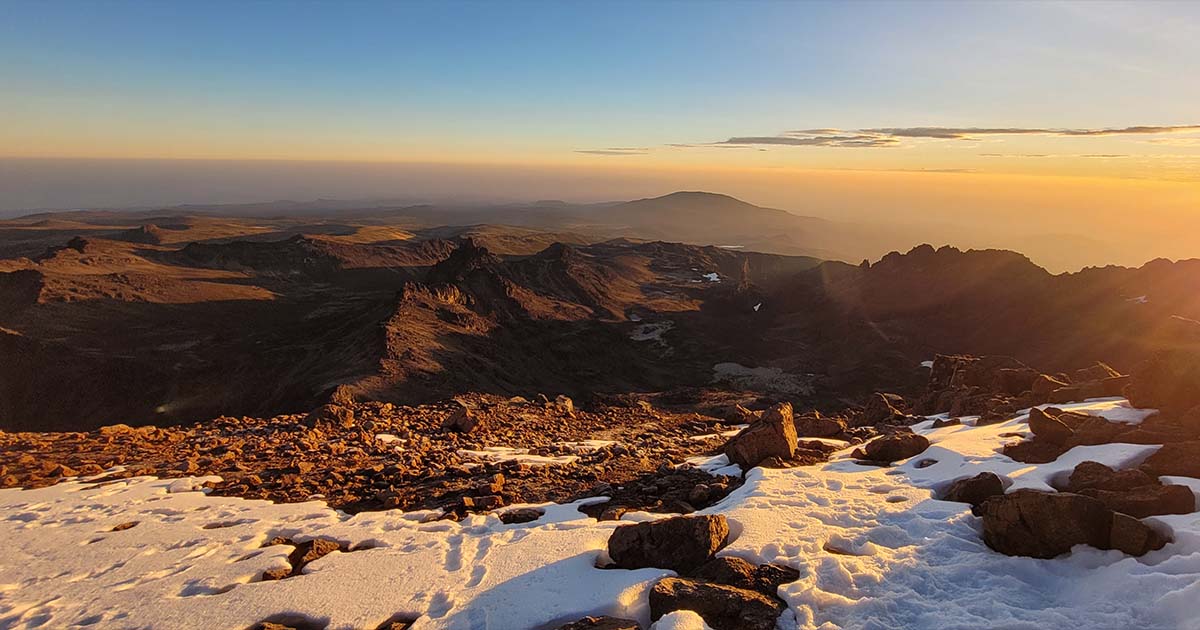 The sunrise view from a snowy mountain peak with rocks in the foreground