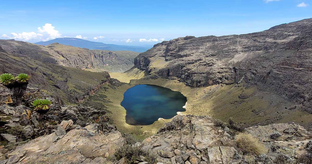 A circular lake surrounded by steep cliffs and mountains under a clear sky