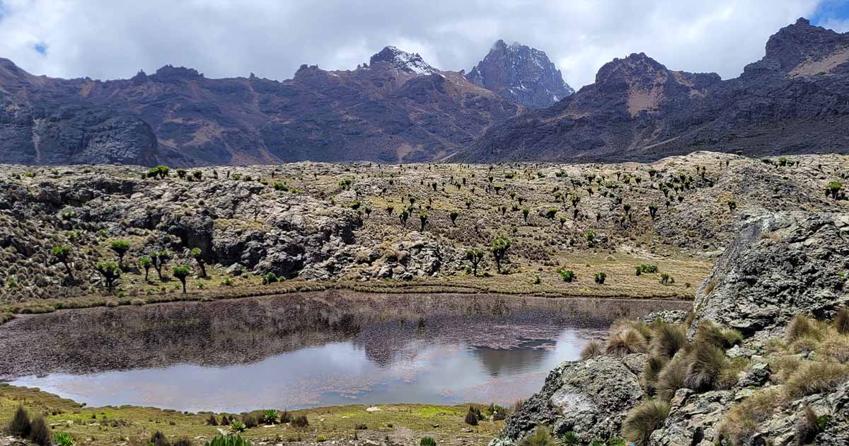 A mountainous landscape with a small lake, rocks, and scattered vegetation under a partly cloudy sky