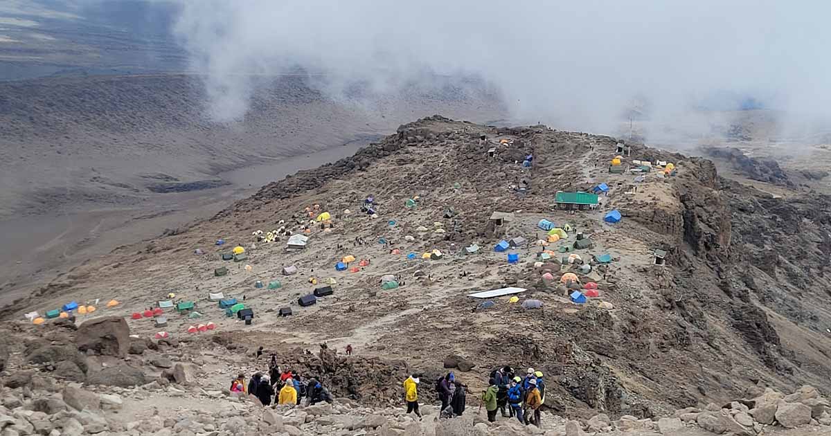 A crowded Barafu Camp with colorful tents scattered across the rugged terrain under a hazy sky