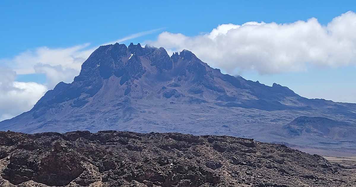 A panoramic view of Mawenzi peak with clouds surrounding the base against a blue sky