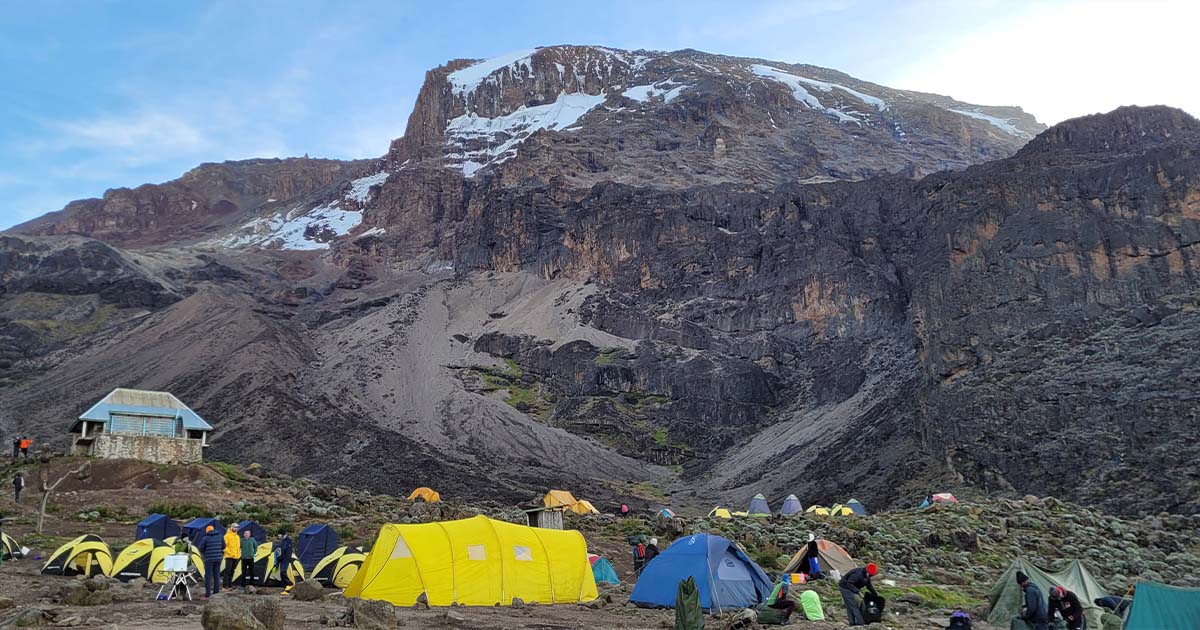 A campsite at Barranco Camp with tents pitched on rocky ground and the mountain looming in the background