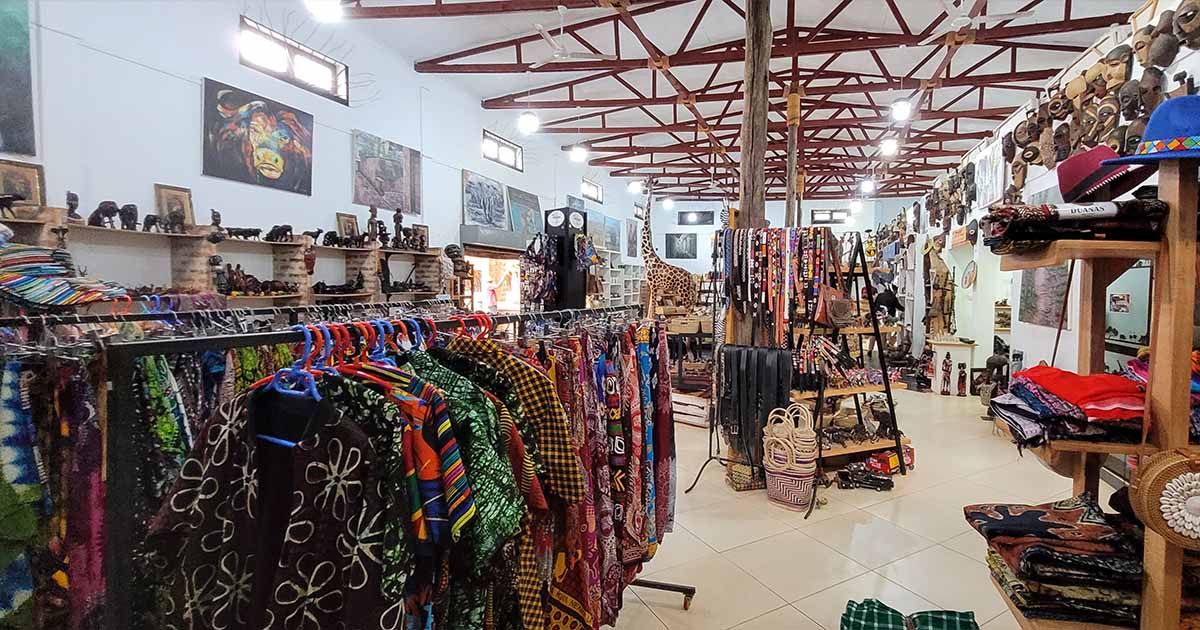 Inside a souvenir shop filled with colorful fabrics, carvings, and paintings, showcasing Tanzanian culture