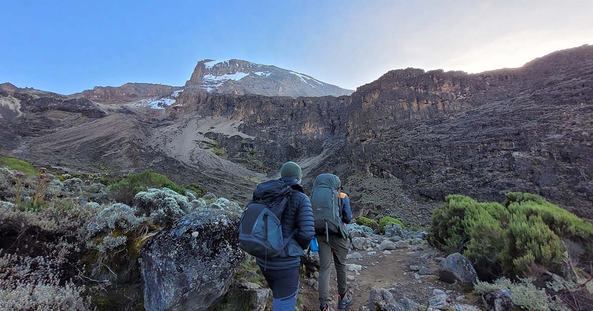 Two hikers with backpacks walking towards the steep slopes of Barranco Wall