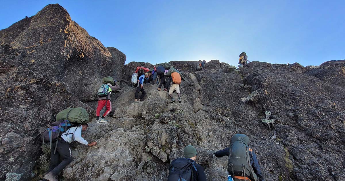 Climbers and Porters navigating a steep, rocky section of Barranco Wall with hands and feet