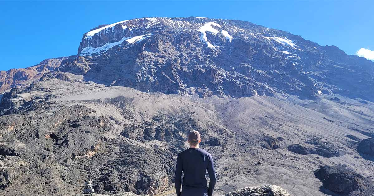 Me facing the snow-capped peak of Kilimanjaro under a clear blue sky