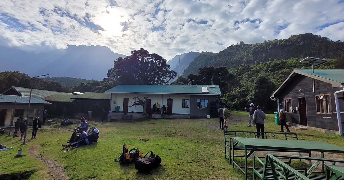 Hikers and staff around the Miriakamba Campsite with huts and Mount Meru in the background