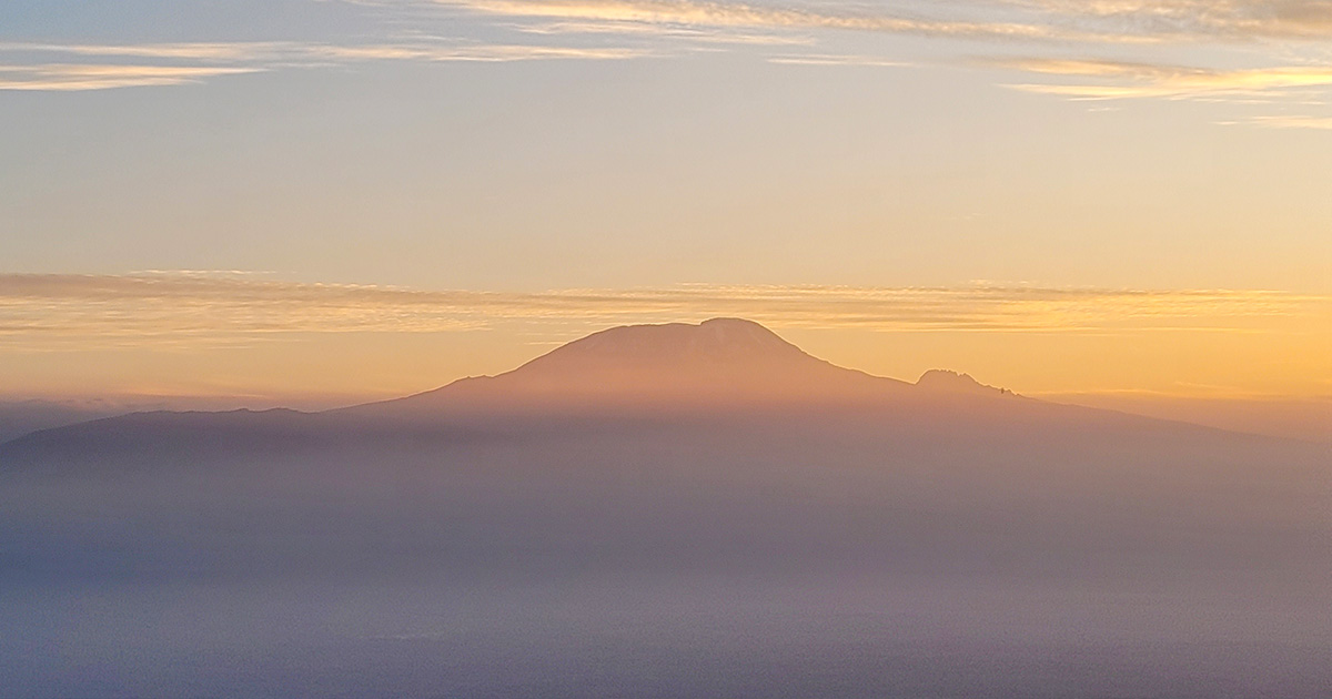 The sun rising over the silhouette of Mount Kilimanjaro against a hazy sky