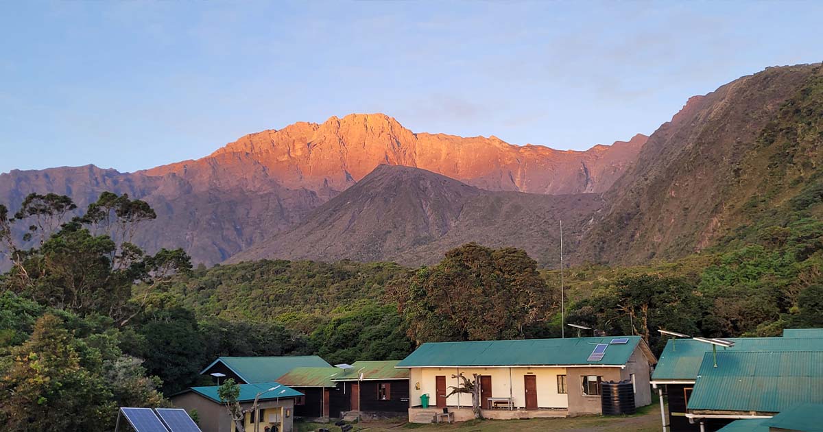 Sunrise illuminating the peak of Mount Meru as seen from a campsite with huts