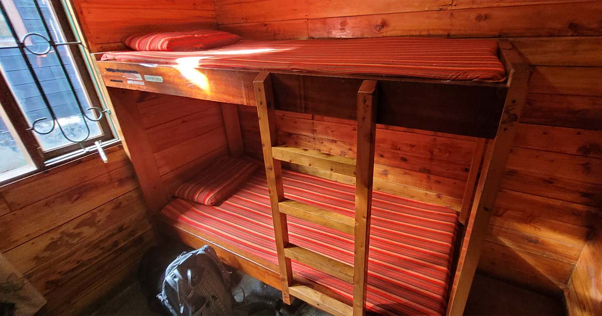 Inside a wooden hut with a bunk bed featuring red striped mattresses