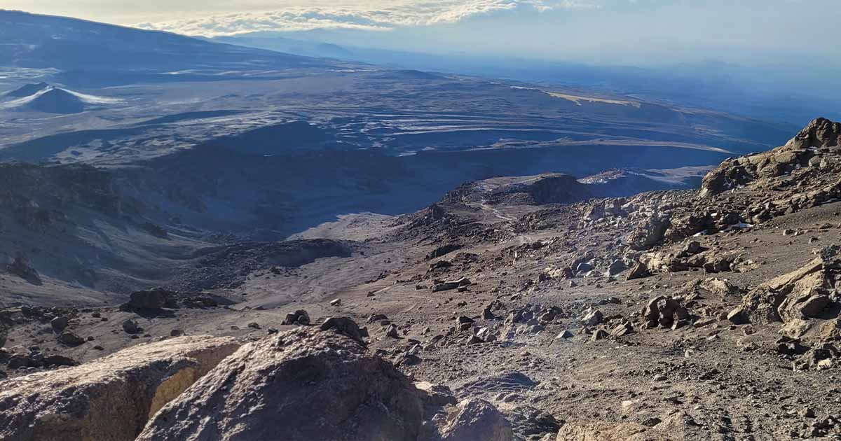 Rocky volcanic terrain with a clear path cutting through; vast plains stretch out in the distance under a bright sky